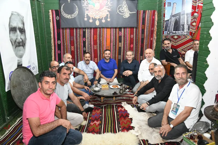 Kilim serili bir odada yerde oturarak sohbet eden kalabalık bir grup