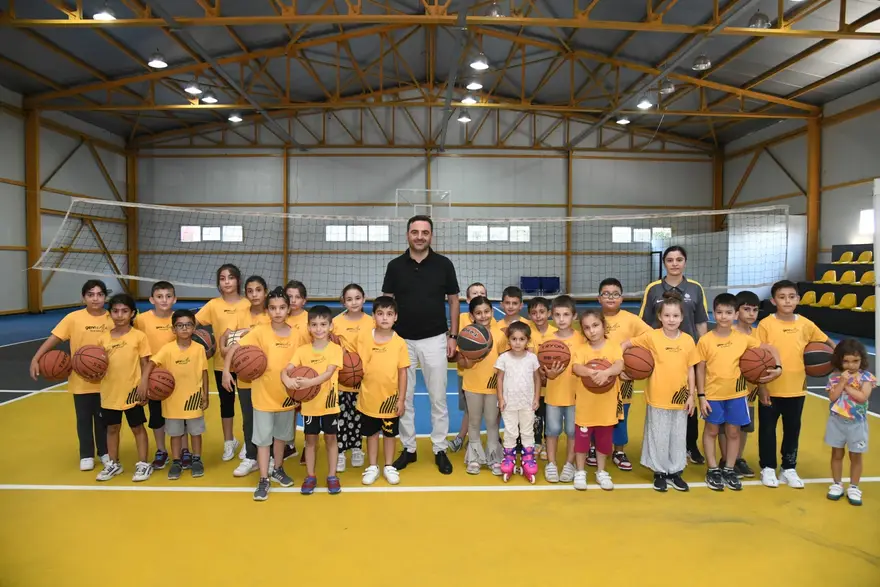 Spor salonunda sarı tişörtlü çocuklar basketbol toplarıyla sıralanmış