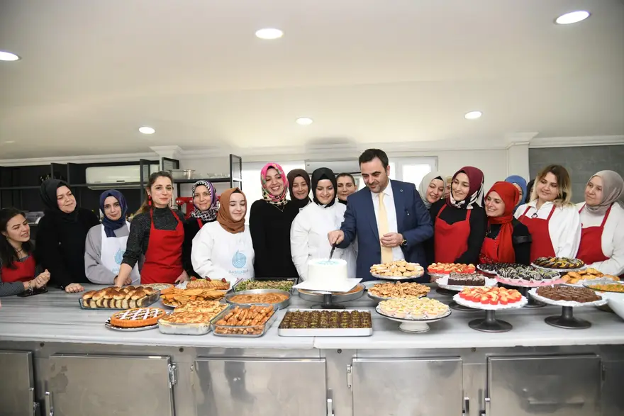 Önlüklü kadınlar ve Başkan Özlü, yemeklerle dolu uzun bir masanın başında